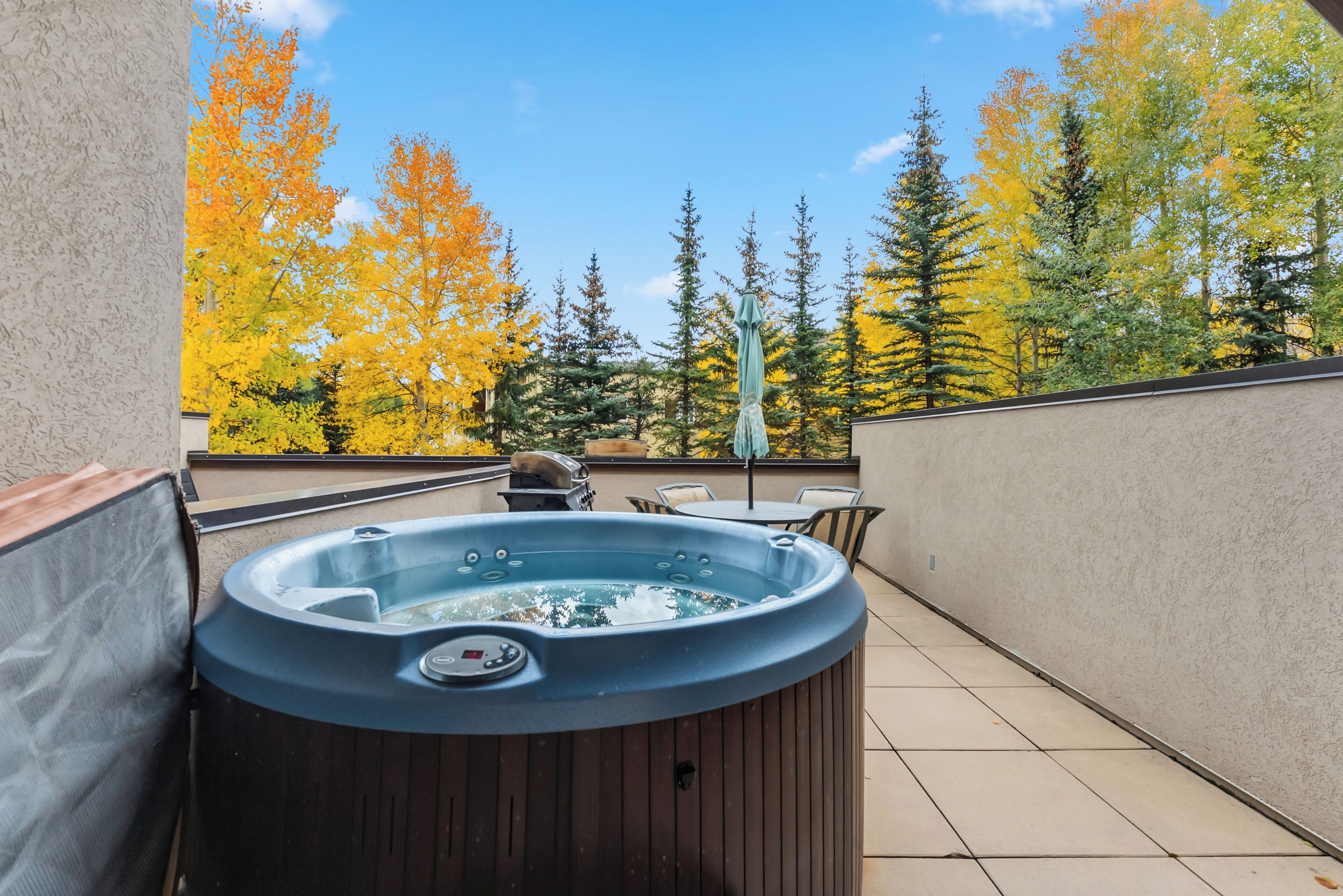 A hot tub on a balcony with a view of autumn trees and a clear sky.