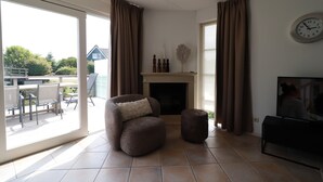 A living room with a fireplace, a sofa, a television, and a dining area with chairs and a table. - Stylish Waterfront Villa With Sauna (Makkum)