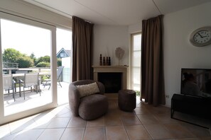 A living room with a fireplace, a sofa, a television, and a dining area with chairs and a table. - Stylish Waterfront Villa With Sauna (Makkum)