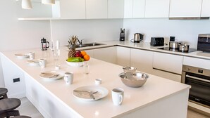 A modern kitchen with white cabinetry, a central island with dining setup, and stainless steel appliances. - 2BR Villa! Private Luxury Escape Overlooking the Caribbean Sea in Antigua! (Urlings)