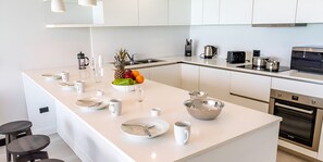 Een moderne keuken met witte kasten, een centraal keukenblok met eettafel en roestvrijstalen apparatuur.