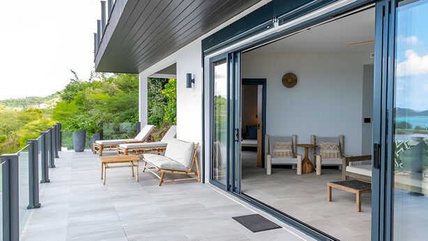 A modern outdoor balcony with a view of the sea, furnished with wooden chairs and a table. - 2BR Villa! Private Luxury Escape Overlooking the Caribbean Sea in Antigua! (Urlings)
