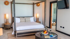 A modern hotel room with a four-poster bed, two bedside tables with lamps, a round coffee table with magazines and fruit, and a large mirror on the wall. - 2BR Villa! Private Luxury Escape Overlooking the Caribbean Sea in Antigua! (Urlings)