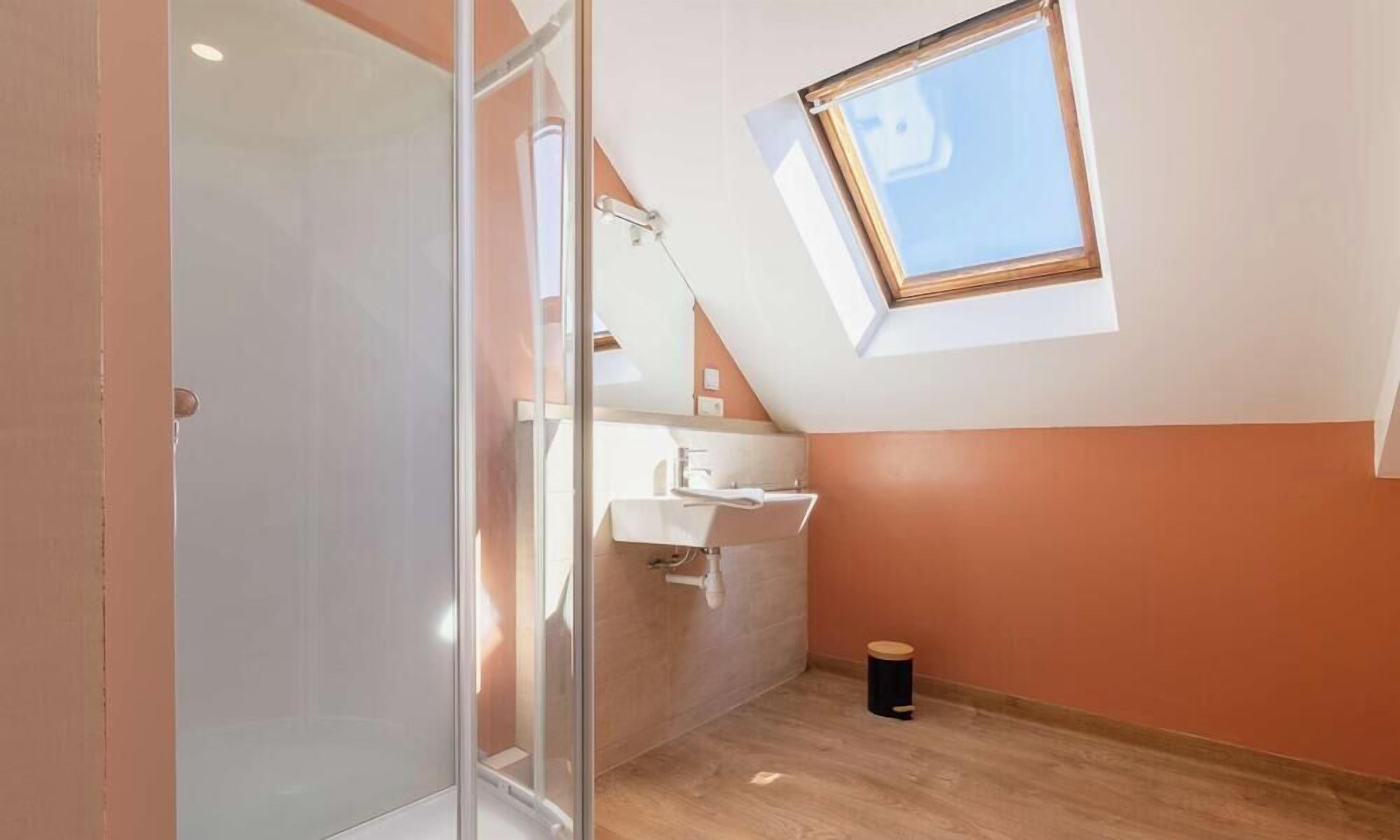 Une salle de bain moderne dotée d’un puits de lumière, d’une douche en verre et d’un lavabo blanc.