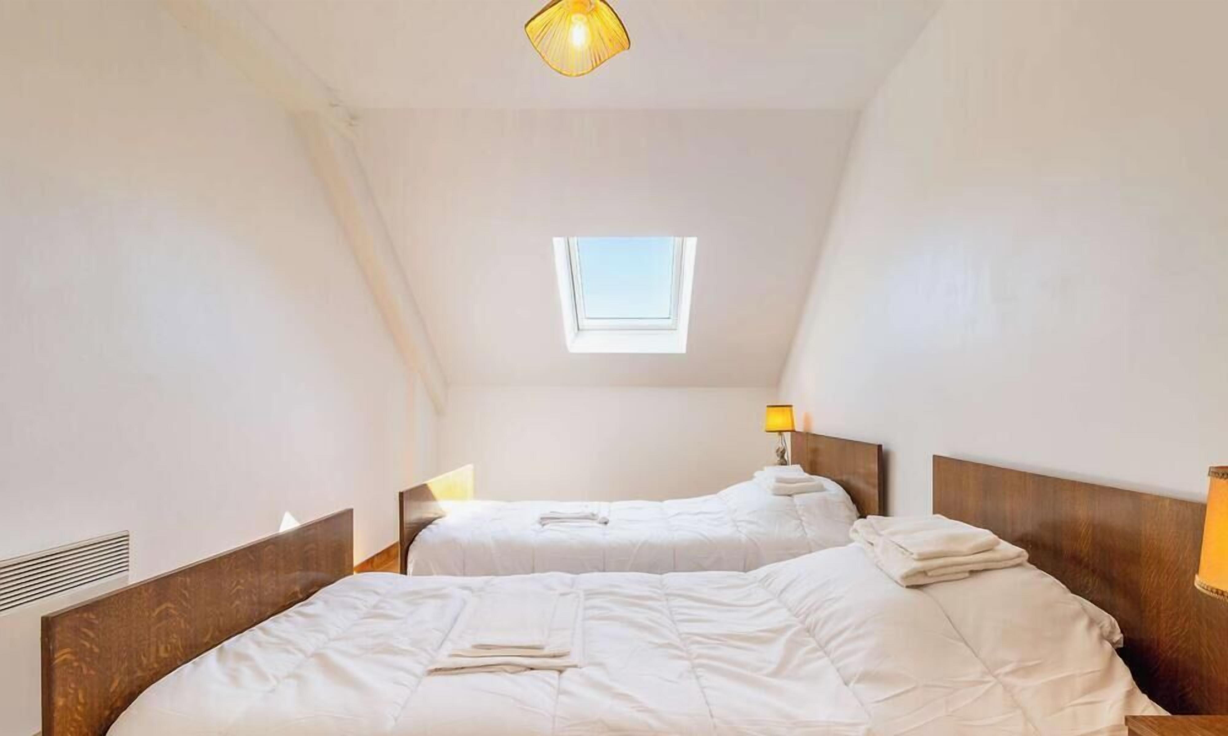 Quarto com duas camas, um claraboia e um lustre.