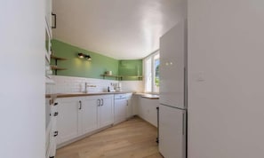 A kitchen with white cabinets, a wooden countertop, and a green wall. - Renovated house between Sables-d’Or and Cap Fréhel | 8 guests | Ref 215 (PLURIEN)