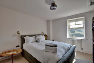 Un dormitorio con cama, lámpara de noche, ventana y radiador.