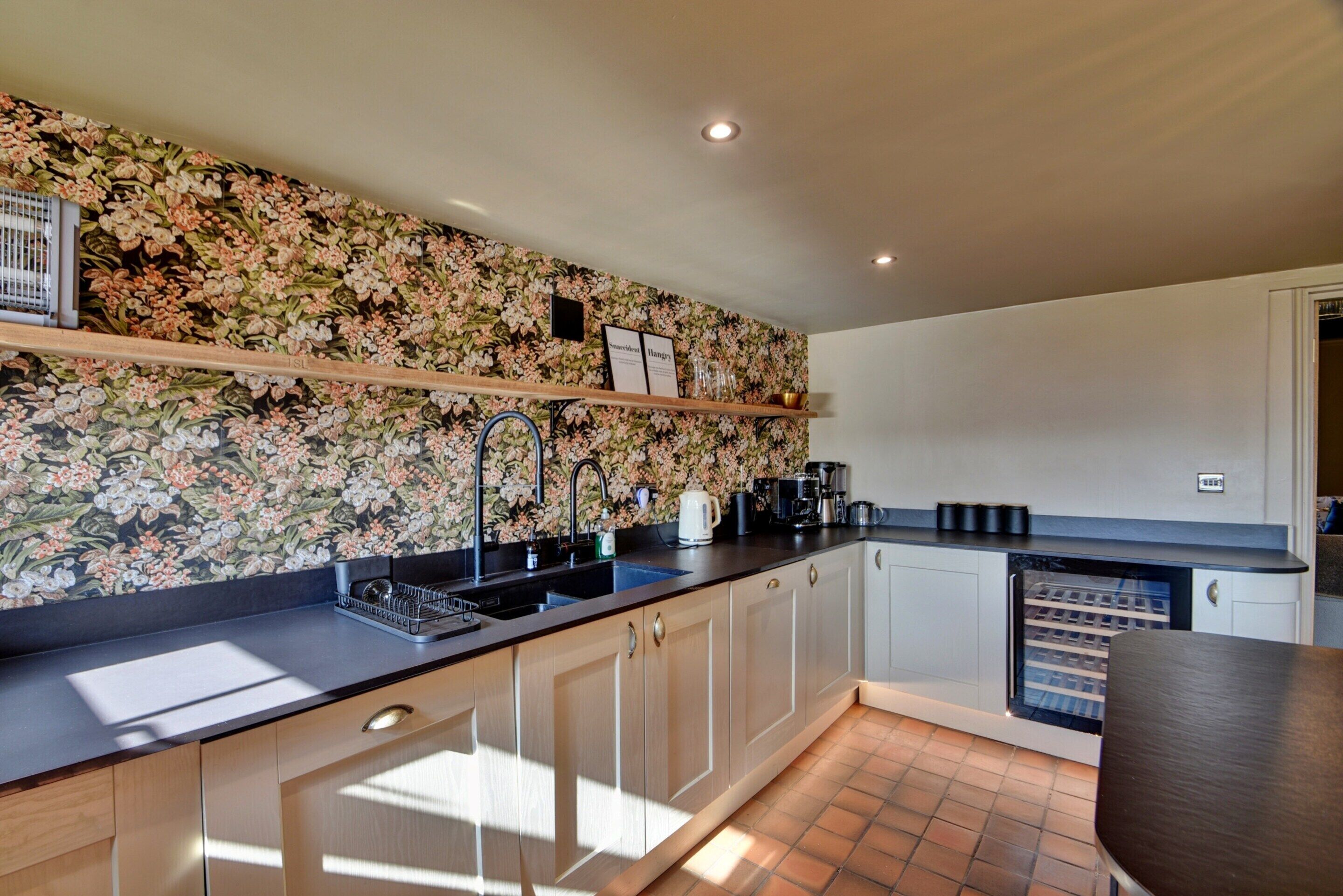 Una cocina moderna con un backsplash floral, lavavajillas integrado y una estación de café.
