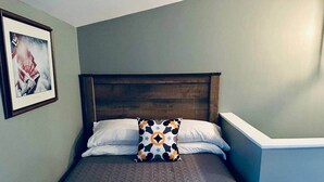 Una cama individual con cabecera, almohadas blancas y un cojín decorativo estampado.