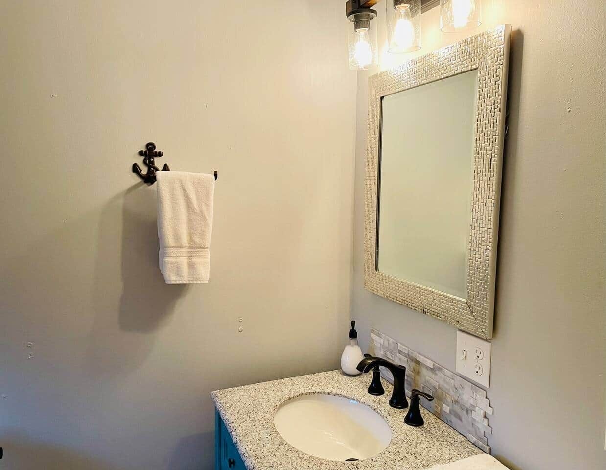 Une salle de bain équipée d’un lavabo, d’un miroir, d’un porte-serviettes et d’un luminaire fixé au mur.