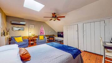 Un dormitorio con cama, escritorio, silla, armario, ventilador de techo y tragaluz.