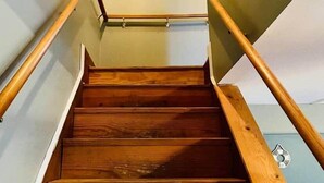 Una escalera de madera con barandilla, un cuadro en la pared y un interruptor de luz.