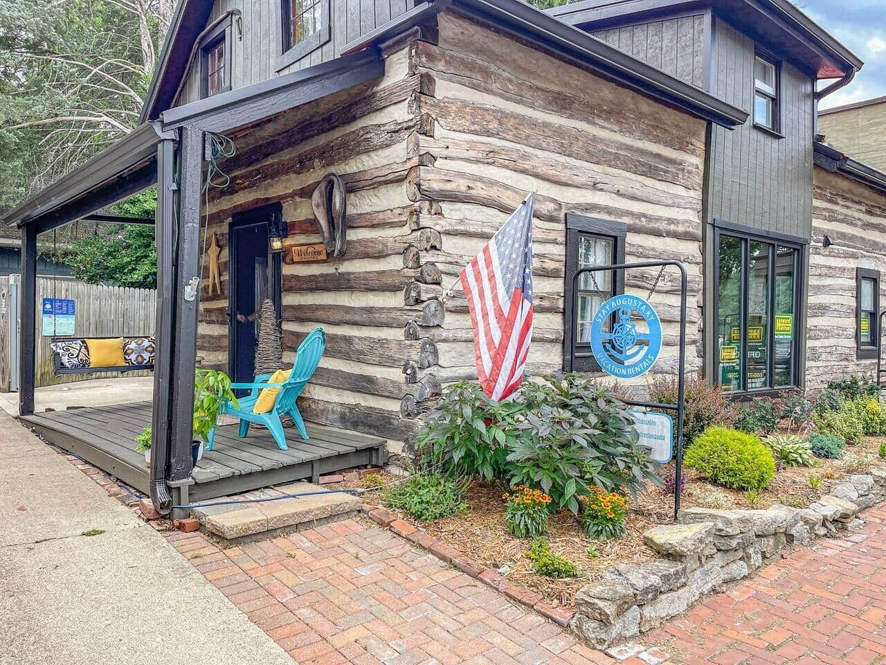 A log cabin with a porch, a flag, and a sign for a rental business.
