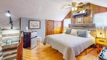 A bedroom with a bed, wooden walls, a ceiling fan, a desk, and a small window.