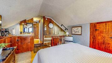 A bedroom with a sloped ceiling, wooden furniture, a bed, a desk, and a wall clock.