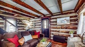 Ein Holzblockhaus-Innenraum mit einem braunen Ledersofa, einem kleinen Tisch mit einer Pflanze und einem Kamin aus Stein.