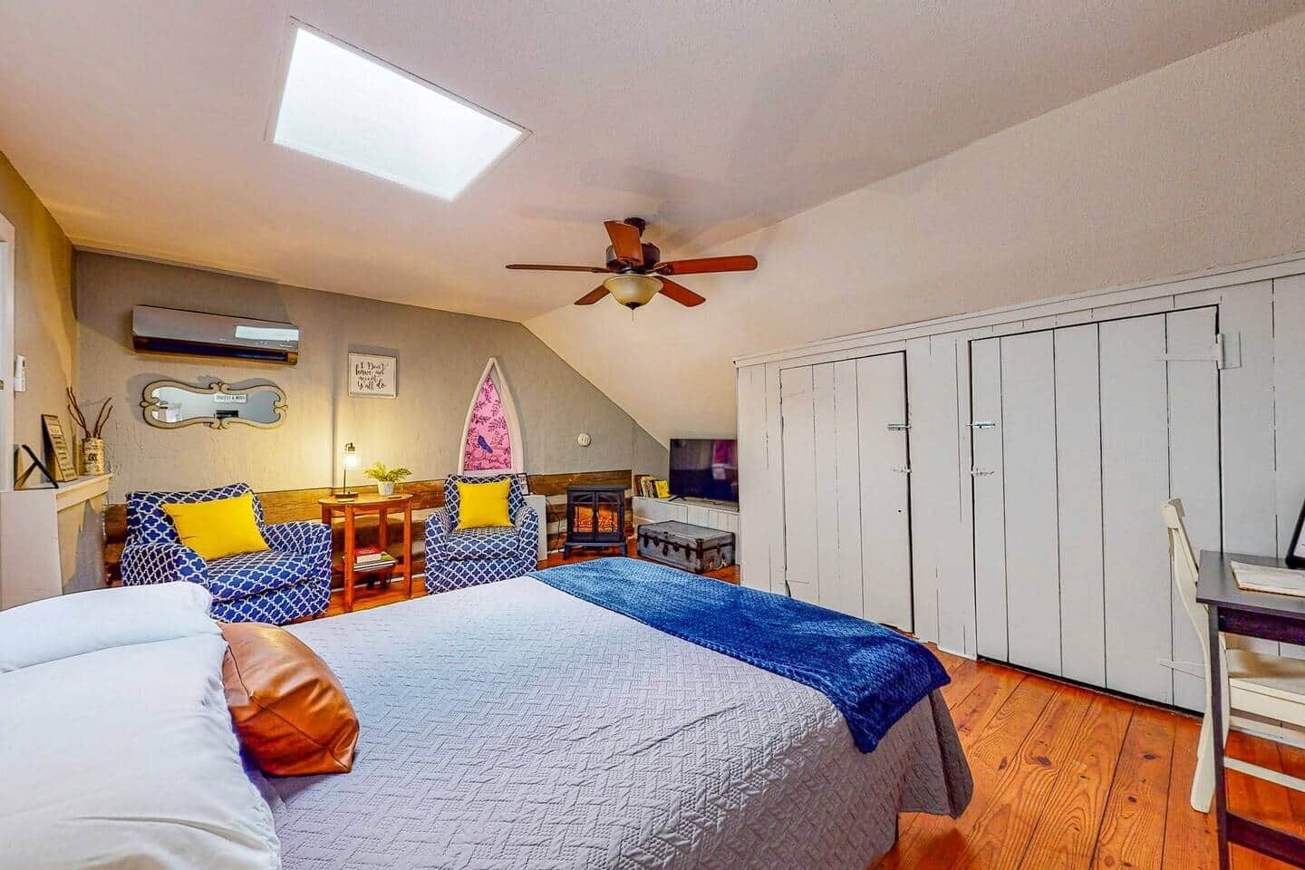 Ein Schlafzimmer mit einem Bett, einem Schreibtisch, einem Stuhl, einem Kleiderschrank, einem Deckenventilator und einem Oberlicht.