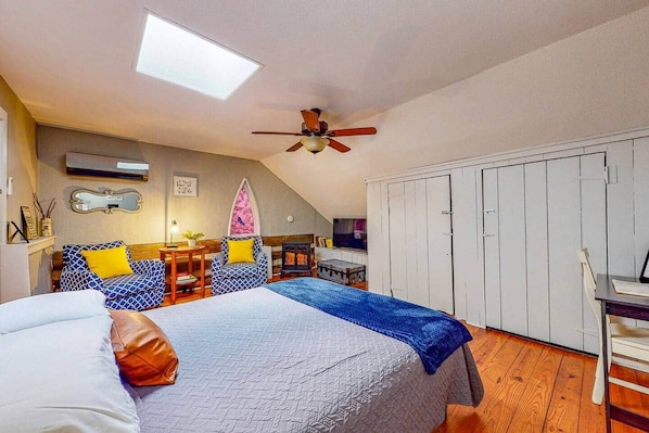 A bedroom with a bed, a desk, a chair, a wardrobe, a ceiling fan, and a skylight.