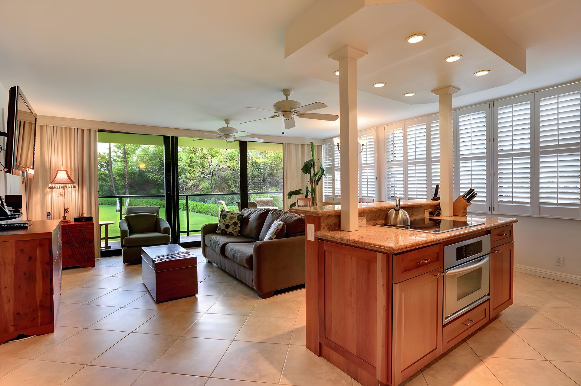 A modern kitchen with a central island, a dining area with a sofa and chairs, and large windows with blinds.