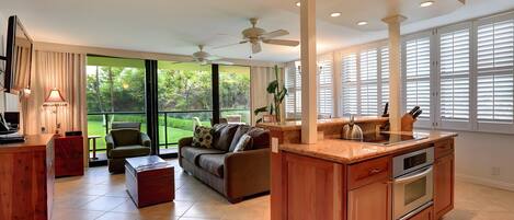 A modern kitchen with a central island, a dining area with a sofa and chairs, and large windows with blinds.