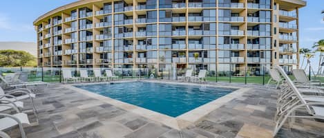 Un hotel de varios pisos con zona de piscina, incluyendo sillas de descanso y una vista despejada del océano.