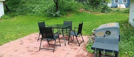A patio with a grill, a table, and chairs.