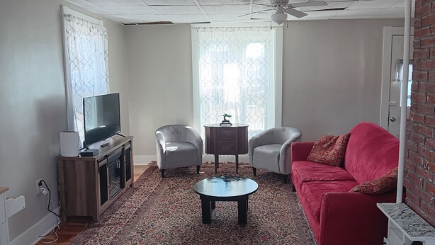 A living room with a television, two chairs, a red sofa, a coffee table, and a patterned rug. - Newly renovated, New England 3-bedroom home in Skowhegan. (Skowhegan)