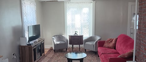 A living room with a television, two chairs, a red sofa, a coffee table, and a patterned rug.