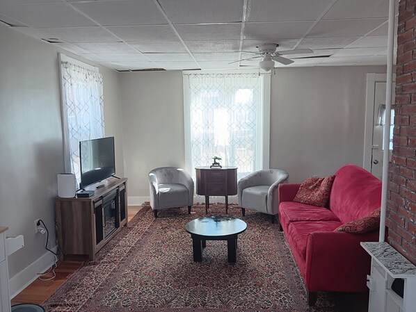 A living room with a television, two chairs, a red sofa, a coffee table, and a patterned rug.