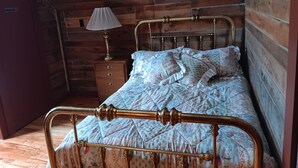 A wooden cabin room with a bed, a nightstand, and a lamp. - Newly renovated, New England 3-bedroom home in Skowhegan. (Skowhegan)
