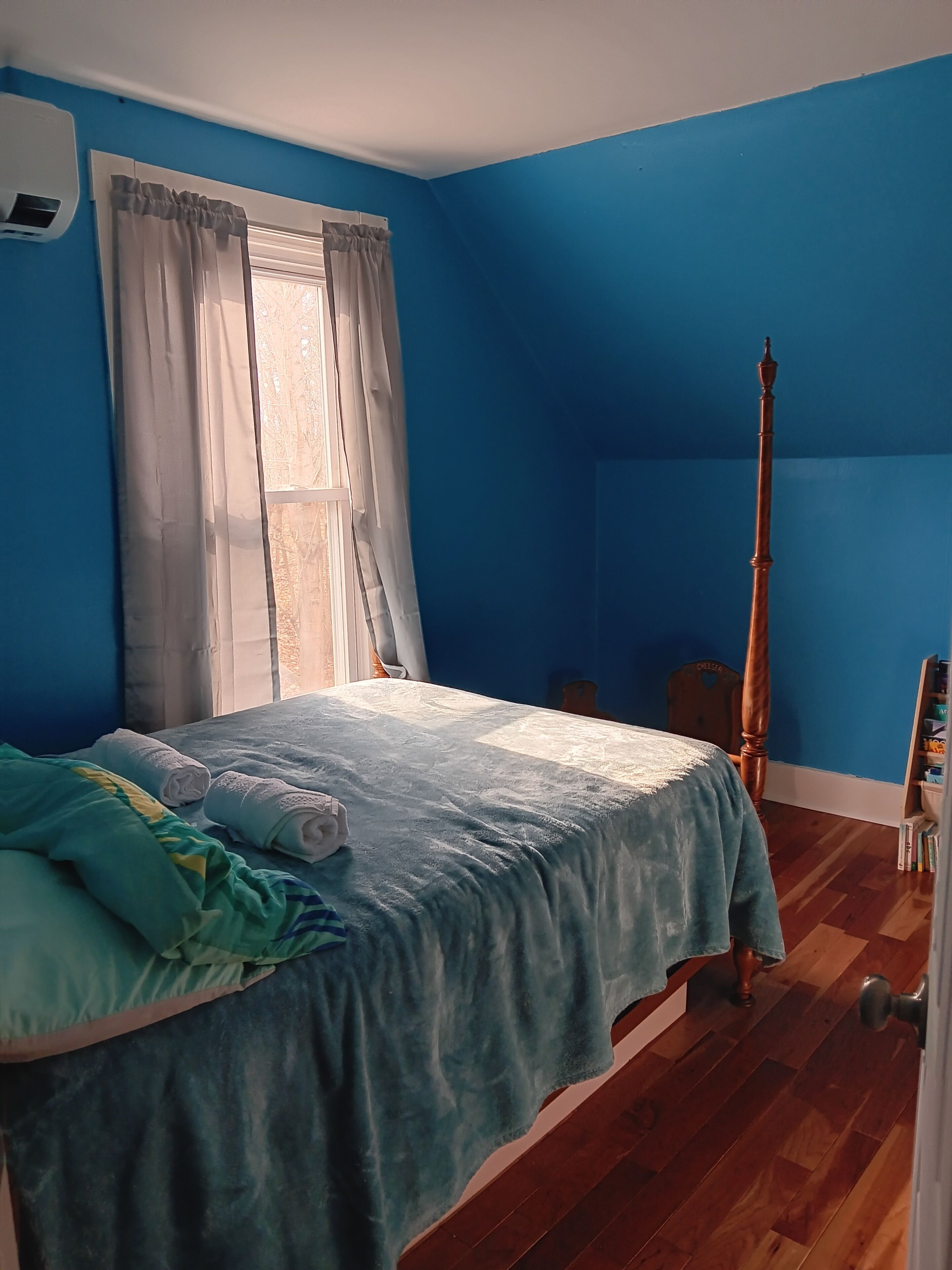 Una stanza con un letto, una finestra con tende, un pavimento in legno e una porta.