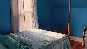 Una stanza con un letto, una finestra con tende, un pavimento in legno e una porta.