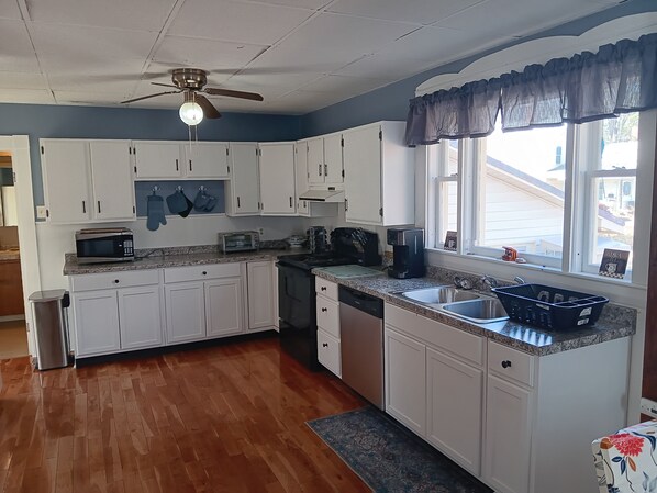 A kitchen with white cabinets, a microwave, a toaster, a coffee maker, and a window with a view of the outside.
