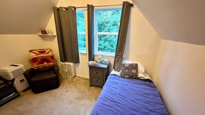 A bedroom with a bed, a chair, a bedside table, a lamp, and a window with curtains.