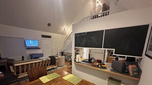 A cozy living room with a wooden dining table, a sofa, a TV, and a kitchen area with a chalkboard.