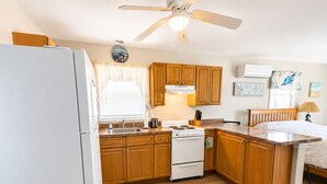 A compact kitchen with wooden cabinets, a white stove, and a ceiling fan.