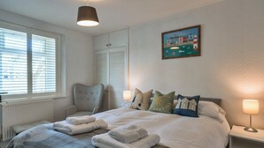 A bedroom with a bed, bedside lamps, a chair, a window with blinds, and a painting on the wall. - 19th Century Cottage Near Brixham Harbour (Brixham)