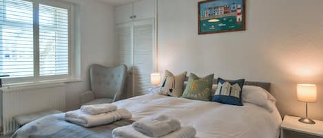 Une chambre à coucher avec un lit, des lampes de chevet, une chaise, une fenêtre avec des stores et un tableau au mur.