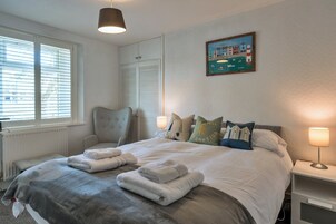 Une chambre à coucher avec un lit, des lampes de chevet, une chaise, une fenêtre avec des stores et un tableau au mur.