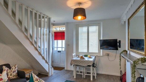 A living room with a staircase, a dining area with a table set for breakfast, a TV mounted on the wall, and a large mirror. - 19th Century Cottage Near Brixham Harbour (Brixham)
