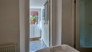 A narrow hallway leading to a room with a bed, a door, and a view of an outdoor area with a stone wall and greenery. - 19th Century Cottage Near Brixham Harbour (Brixham)