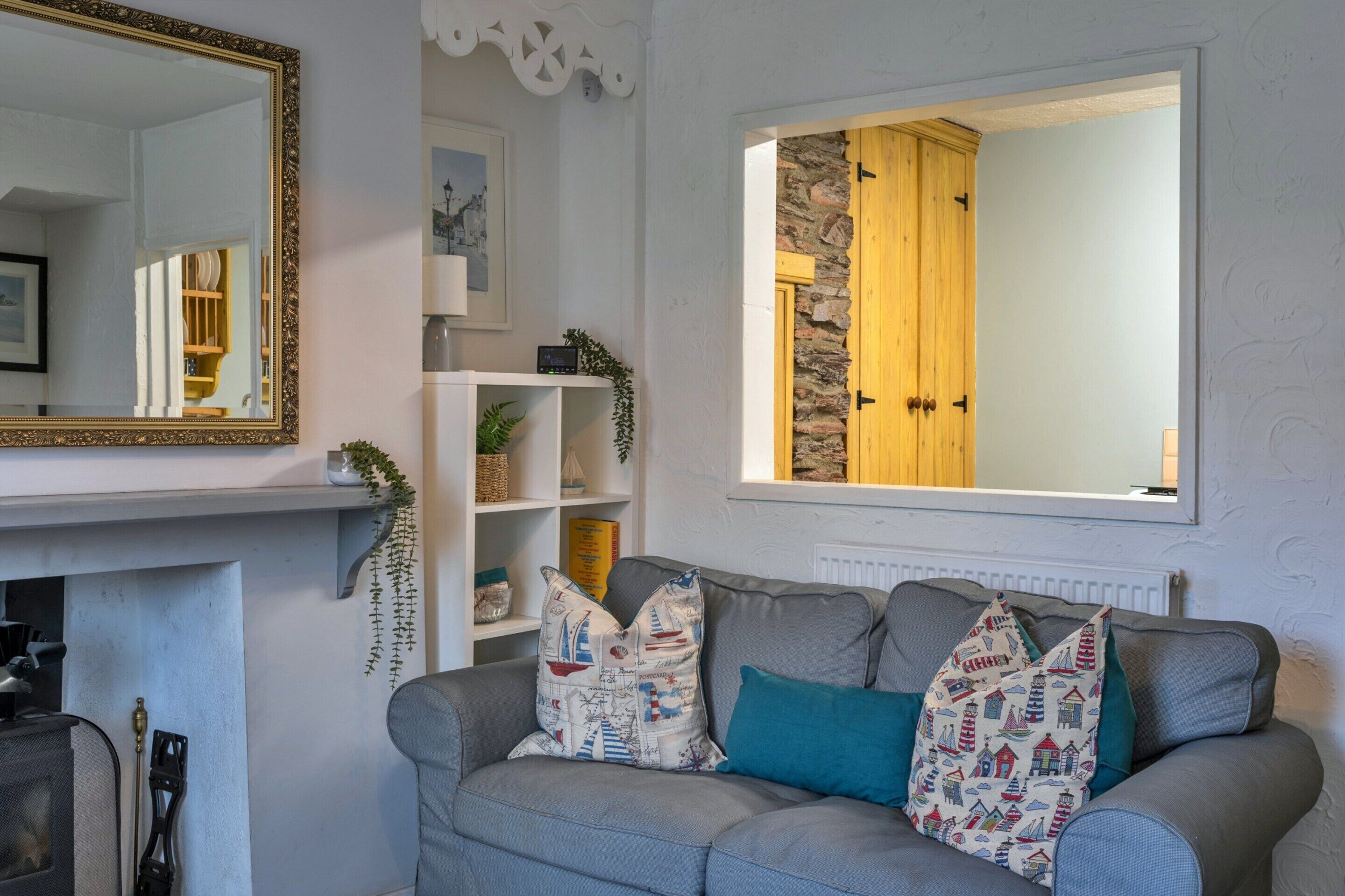 A living room with a grey sofa, decorative pillows, a white fireplace, a large mirror, and a stone wall with a wooden door.
