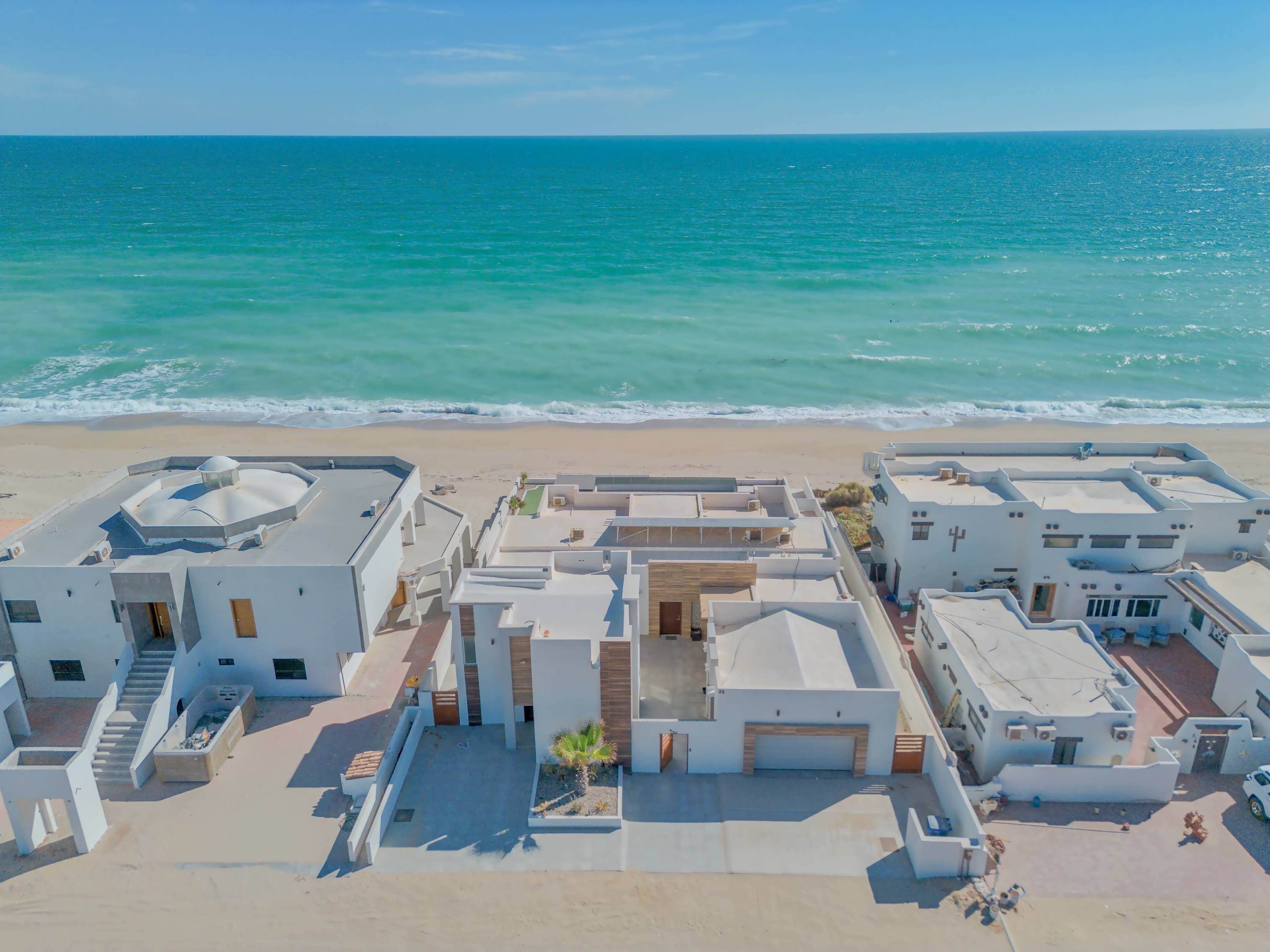 Una zona residencial costera con arquitectura moderna, que presenta edificios de techo plano, un patio central y una playa al fondo.