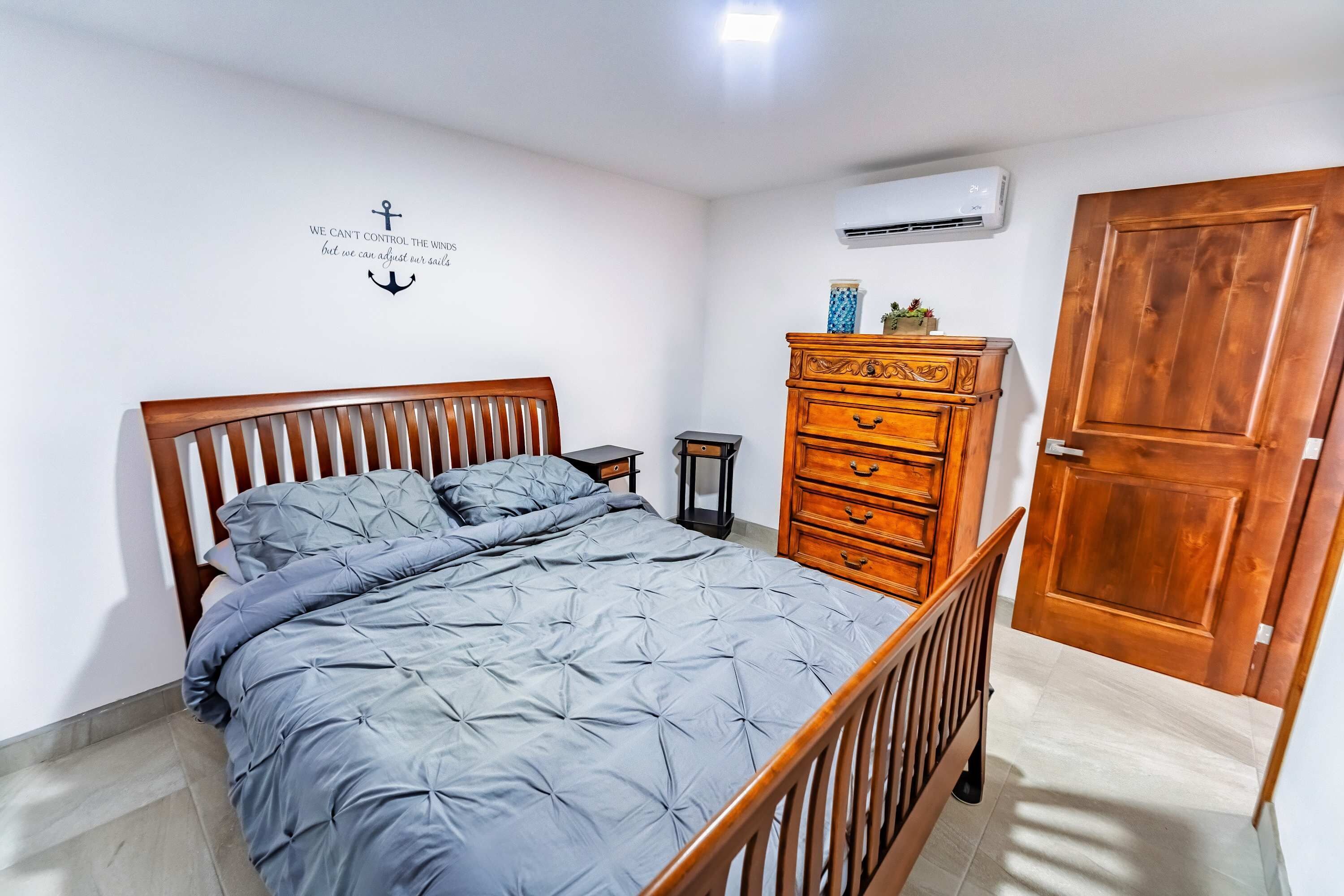 A bedroom with a bed, dresser, nightstand, and an air conditioning unit.