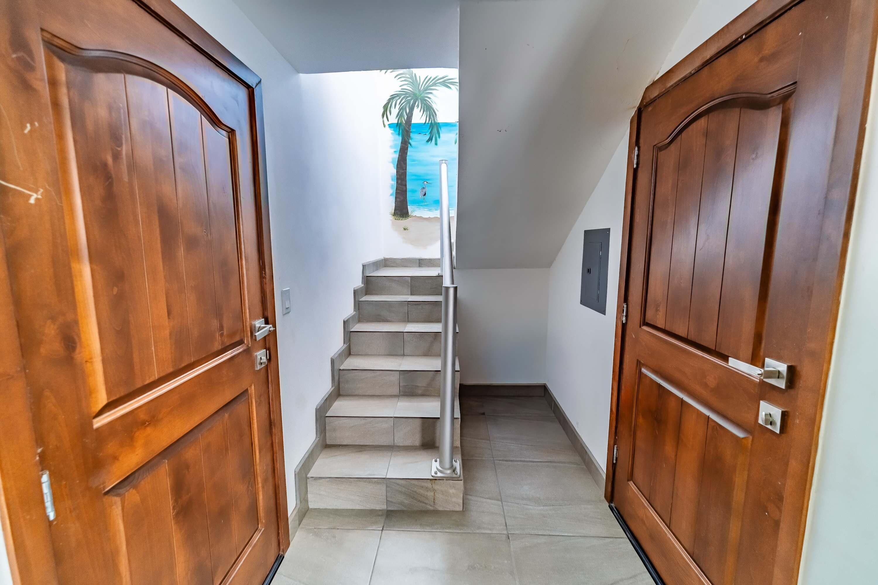 Un pasillo con puertas de madera, una escalera y un cuadro en la pared que muestra una playa.