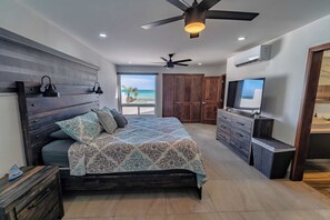 Ein Schlafzimmer mit einem großen Bett, einem Deckenventilator, einem Fernseher und Blick auf den Ozean.