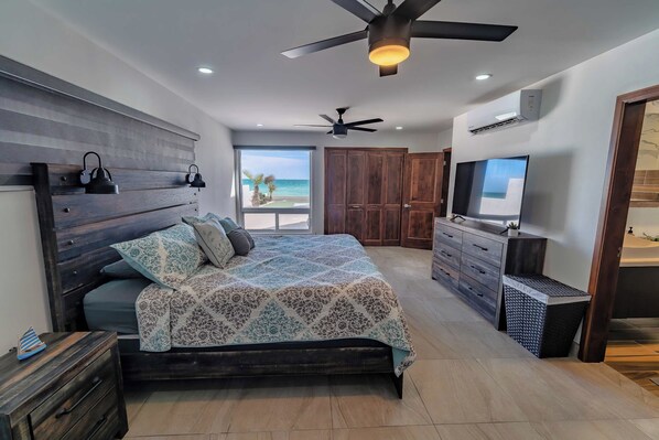 Ein Schlafzimmer mit einem großen Bett, einem Deckenventilator, einem Fernseher und Blick auf den Ozean.