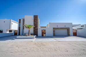 A modern residential building with a garage, a palm tree, and a clear sky. - Casa Mareas | Luxury Beachfront Estate | Spa | 6BR (Playa Encanto)
