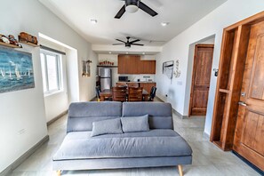 Ein modernes Wohnzimmer mit einem grauen Sofa, einem Deckenventilator und einer Küche im Hintergrund.
