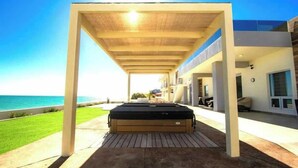 Un espace extérieur abrité avec un jacuzzi, une vue sur la mer et un bâtiment moderne en arrière-plan.
